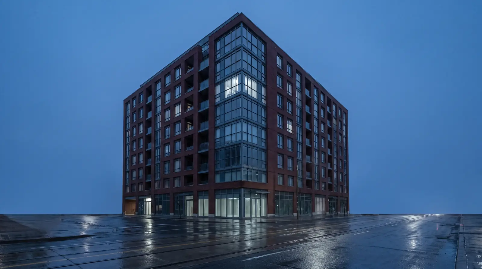 Ten-storey brick and glass rental apartment building on a Toronto street corner at blue hour